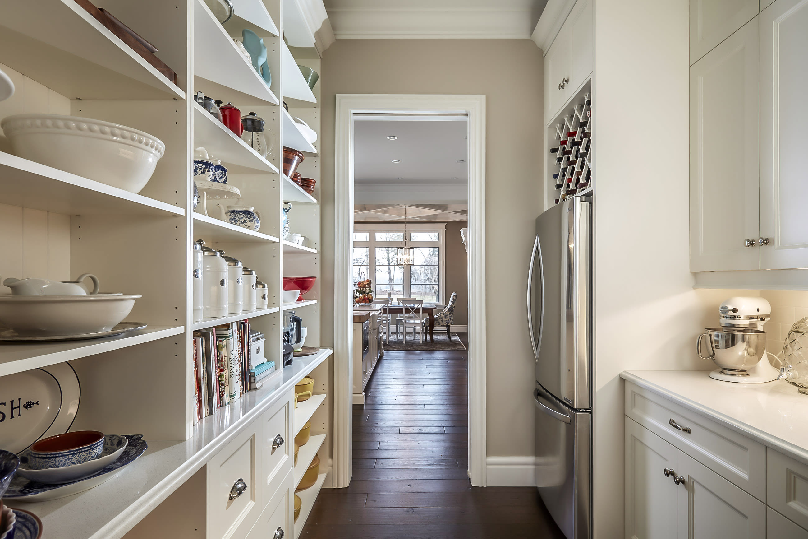 A butlers pantry with open shelving and wine rack above fridge