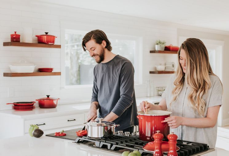 Man and woman in a kitchen with red cookware