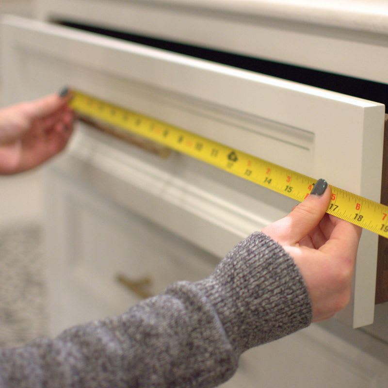 Close up of person holding measuring tape against cabinet